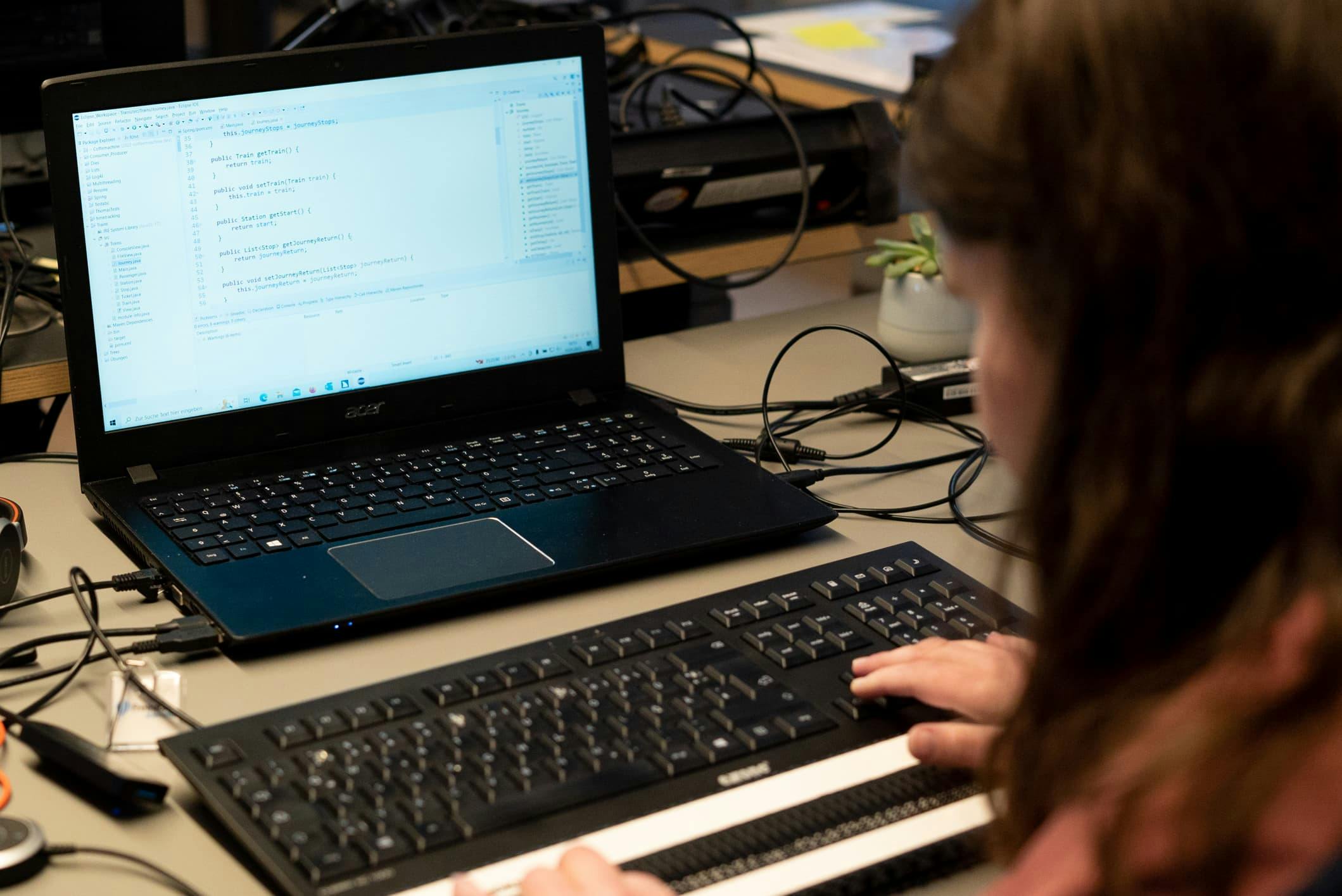 Melanie schreibt Code am Computer, ihre Hände sind auf der Braille-Tastatur